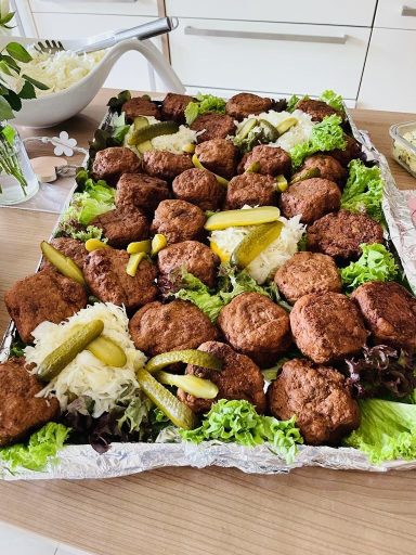 Fleischbällchen auf einem Blech mit Salat und Gurken serviert.