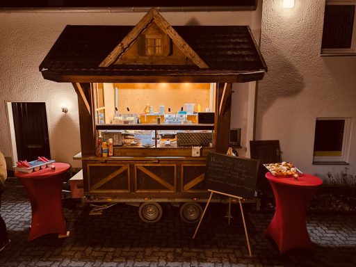 Ein gemütlicher Verkaufsstand mit rotem Tisch und dekorativem Holzaufbau bei Nacht.