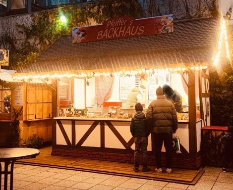 Holzhütte mit Lichtern, in der zwei Personen bei einem Verkaufsstand stehen.