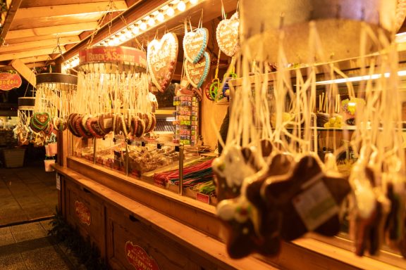 Bunte Lebkuchenherzen und Süßigkeiten hängen an einem Stand auf einem Weihnachtsmarkt.