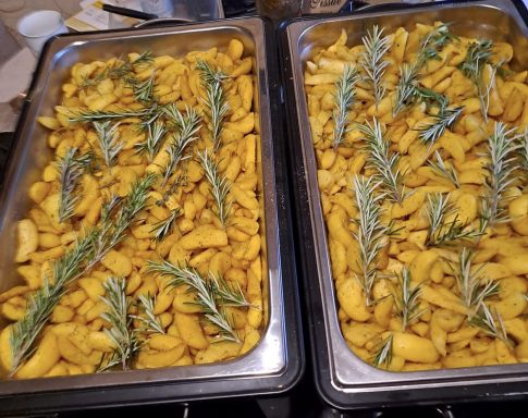 Geröstete Kartoffeln mit Rosmarinzweigen in zwei großen Edelstahlblechen.