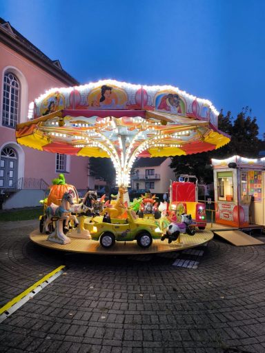 Ein beleuchtetes Karussell mit verschiedenen Fahrzeugen und bunten Figuren.