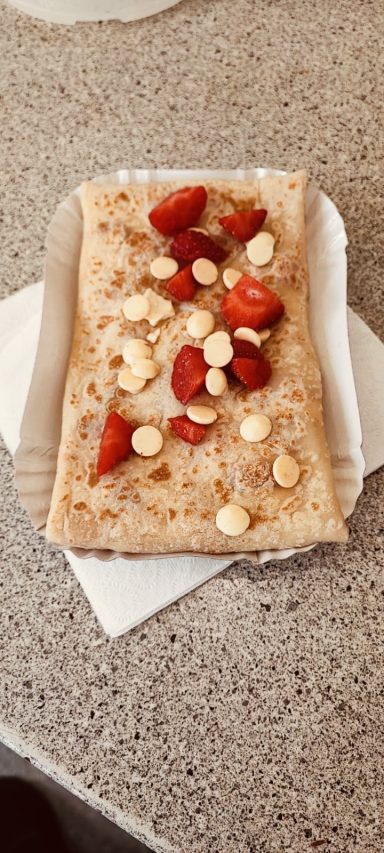 Pfannkuchen mit Erdbeeren und Bananenstücken, auf einem weißen Papier platziert.