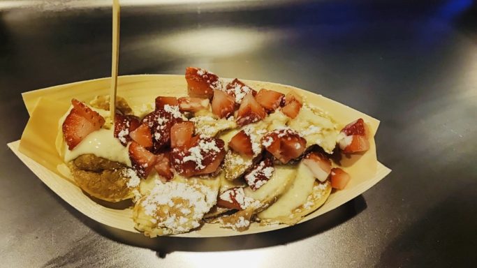 Ein Teller mit Waffeln, Erdbeeren und Schokoladensauce, garniert mit Puderzucker.