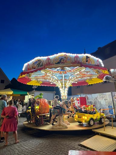Karussell mit bunten Lichtern und Fahrgeschäften auf einem Festplatz bei Nacht.