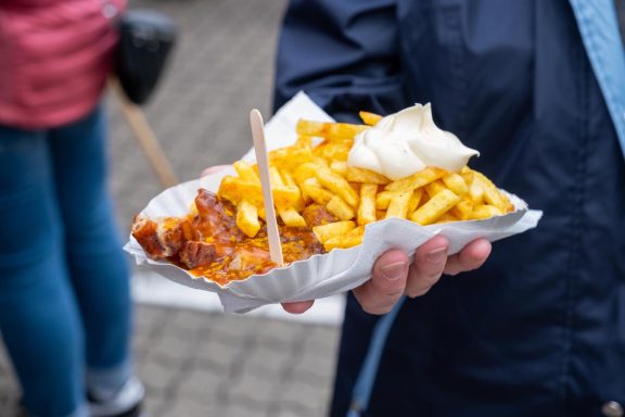 Pommes mit Sauce und einem Klecks Mayonnaise in einer Pappschale, handgehalten.