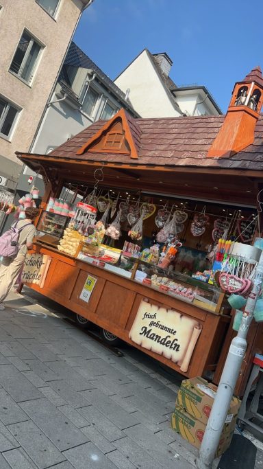 Marktstand mit bunten Waren, Fleisch und regionalen Spezialitäten unter blauem Himmel.