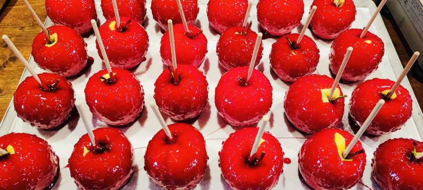 Rote Zuckeräpfel auf einem Tablett, dekoriert mit bunten Stäbchen.
